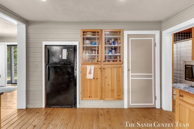 7120 Quarterline Rd, Spring Lake, MI 49456 - kitchen featuring freestanding refrigerator, light wood-style flooring, glass insert cabinets, and wood walls