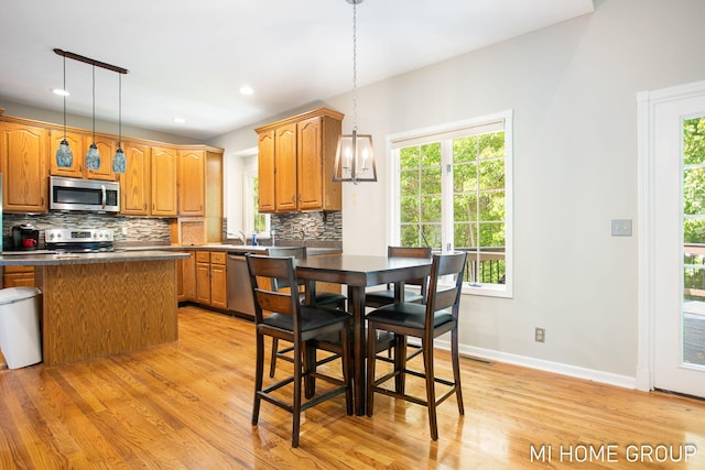 2103 Woodlark Dr, Holland, MI 49424 - kitchen featuring appliances with stainless steel finishes, light wood-style flooring, backsplash, dark countertops, and pendant lighting