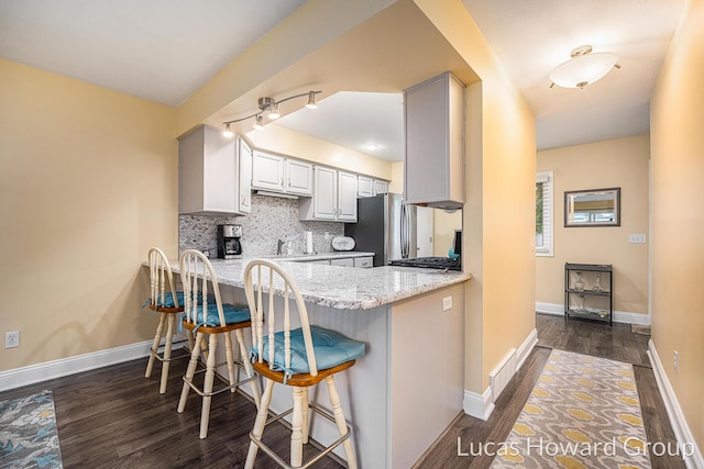 5228 Green Meadow Rd, Kalamazoo, MI 49009 - kitchen featuring freestanding refrigerator, dark wood-type flooring, a peninsula, tasteful backsplash, and light stone counters