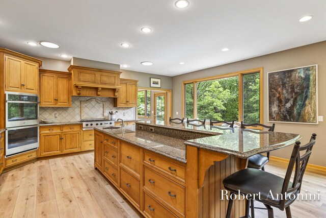 6374 Blakely Dr NE, Rockford, MI 49341 - kitchen with stainless steel double oven, a sink, a kitchen breakfast bar, light wood-style floors, and tasteful backsplash