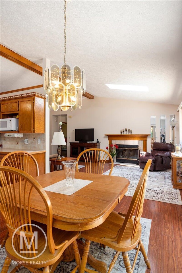 9057 Vergennes St SE, Ada, MI 49301 - dining space featuring a textured ceiling, beam ceiling, a chandelier, dark wood-style floors, and a tile fireplace