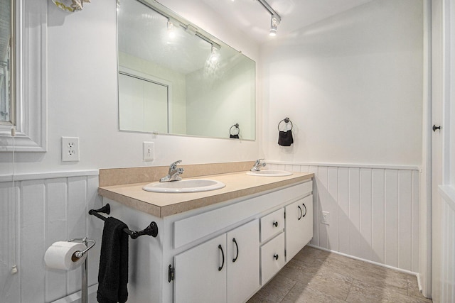 8994 Lenhards Lndg, Clarksville, MI 48815 - bathroom featuring track lighting, double vanity, a wainscoted wall, and a decorative wall