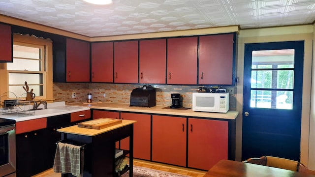 8424 3rd St, Onekama, MI 49675 - kitchen featuring white microwave, red cabinets, light countertops, decorative backsplash, and an ornate ceiling