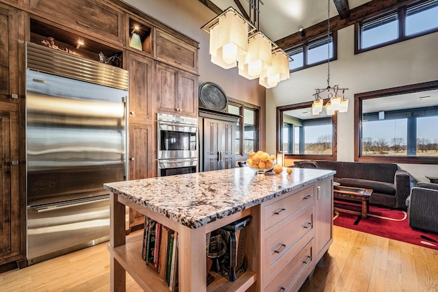 10258 Burgoyne Rd, Berrien Springs, MI 49103 - kitchen featuring appliances with stainless steel finishes, open shelves, light stone counters, light wood-style floors, and a towering ceiling