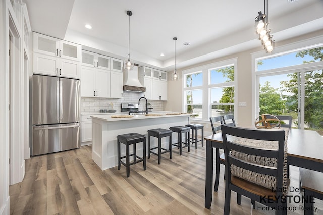 11012 Riverview Dr, Big Rapids, MI 49307 - kitchen with freestanding refrigerator, custom exhaust hood, tasteful backsplash, light countertops, and a center island with sink