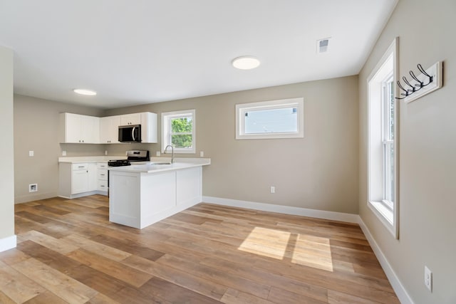 307 N Perrine St, Jackson, MI 49201 - kitchen with stainless steel appliances, a peninsula, light wood-style floors, light countertops, and white cabinetry