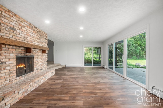 1757 Westlane Dr NE, Grand Rapids, MI 49505 - unfurnished living room featuring a baseboard radiator, baseboard heating, wood finished floors, a brick fireplace, and a textured ceiling
