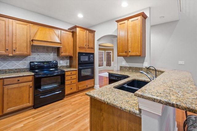 3667 Bay Harbor Dr, Brighton, MI 48114 - kitchen featuring black appliances, custom range hood, arched walkways, light wood-style flooring, and light stone counters