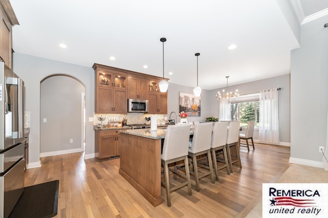 52951 Royal Park Ave, Utica, MI 48315 - kitchen featuring stainless steel appliances, brown cabinets, light wood-style floors, a breakfast bar area, and arched walkways