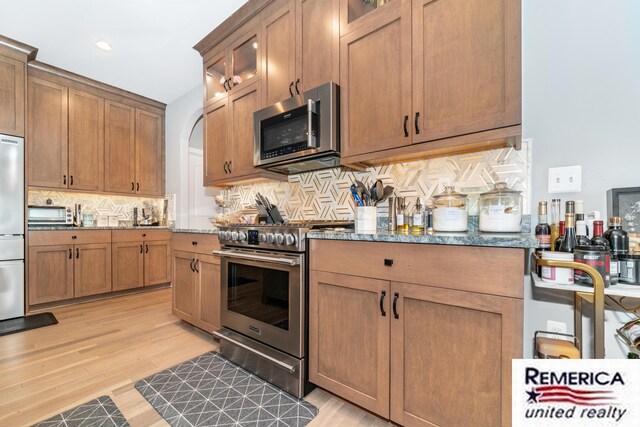 52951 Royal Park Ave, Utica, MI 48315 - kitchen featuring stainless steel appliances, stone countertops, decorative backsplash, glass insert cabinets, and light wood finished floors