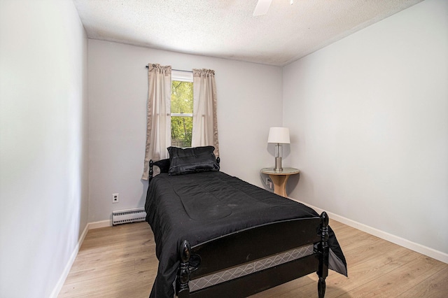 6236 Arbutus, Idlewild, MI 49642 - bedroom featuring a baseboard radiator, light wood-type flooring, a textured ceiling, and a ceiling fan