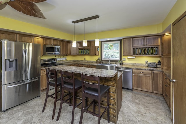 7715 Marquis Dr, Dexter, MI 48130 - kitchen featuring appliances with stainless steel finishes, stone finish flooring, a breakfast bar, a center island, and decorative light fixtures