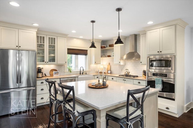 859 Orchard Ave SE, East Grand Rapids, MI 49506 - kitchen with appliances with stainless steel finishes, wall chimney range hood, dark wood-style flooring, light countertops, and a kitchen bar