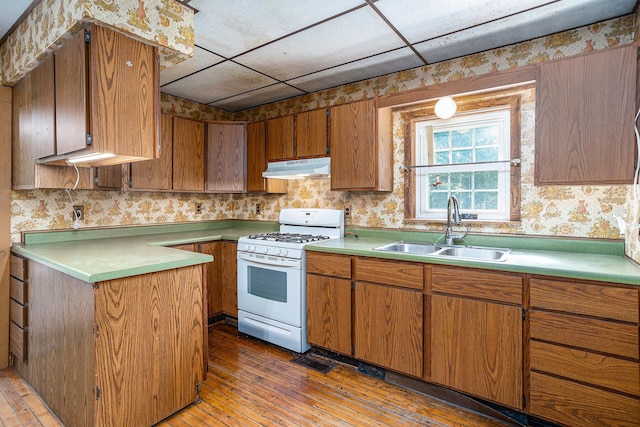 20821 J Dr N, Marshall, MI 49068 - kitchen with gas range gas stove, under cabinet range hood, wallpapered walls, brown cabinetry, and wood-type flooring