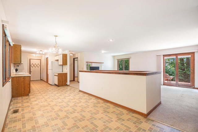 4104 Rurik Dr, Howell, MI 48843 - kitchen featuring freestanding refrigerator, light countertops, a chandelier, brown cabinets, and a fireplace