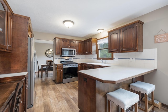 1863 Sunvale Dr SW, Wyoming, MI 49519 - kitchen with appliances with stainless steel finishes, a peninsula, a breakfast bar area, light wood-type flooring, and tasteful backsplash