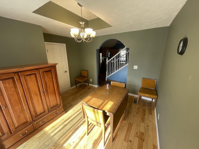 613 James St, Belding, MI 48809 - dining area featuring arched walkways, light wood-type flooring, a chandelier, stairway, and a textured ceiling
