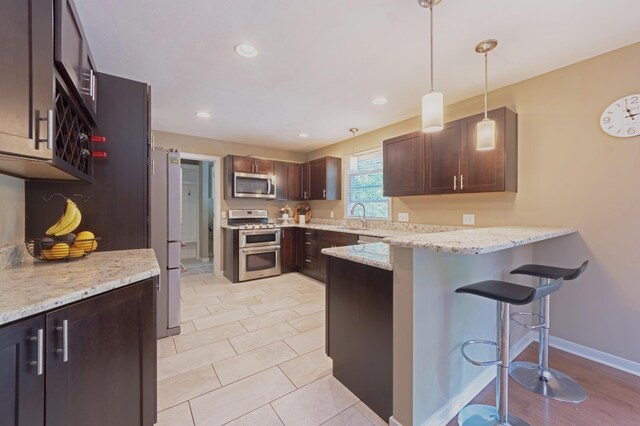 1481 Kristen Path, Saint Joseph, MI 49085 - kitchen featuring appliances with stainless steel finishes, a peninsula, a breakfast bar, decorative light fixtures, and light stone countertops