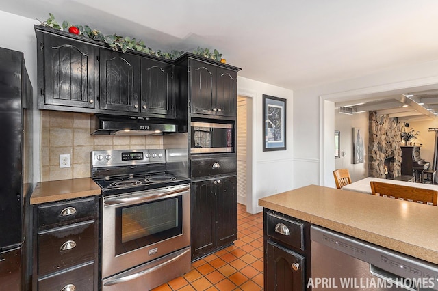 740 Van Raalte Ave, Holland, MI 49423 - kitchen with appliances with stainless steel finishes, under cabinet range hood, decorative backsplash, tile patterned flooring, and dark cabinets
