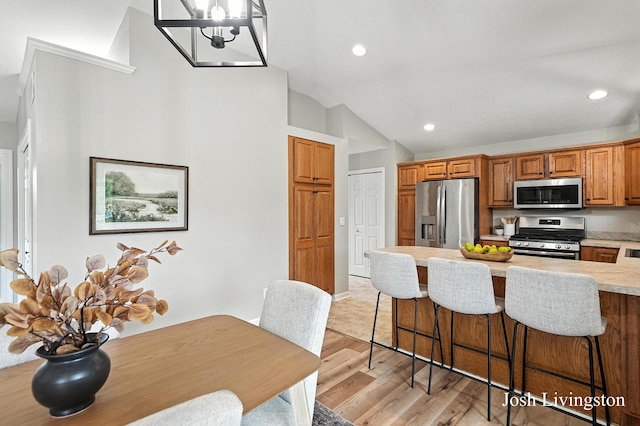 9337 Andrew Farms Dr, Alto, MI 49302 - kitchen featuring appliances with stainless steel finishes, light wood-style flooring, light countertops, a breakfast bar, and lofted ceiling