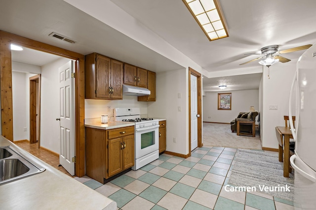 1723 S Sullivan Rd, Ravenna, MI 49451 - kitchen with white appliances, under cabinet range hood, brown cabinetry, light countertops, and ceiling fan