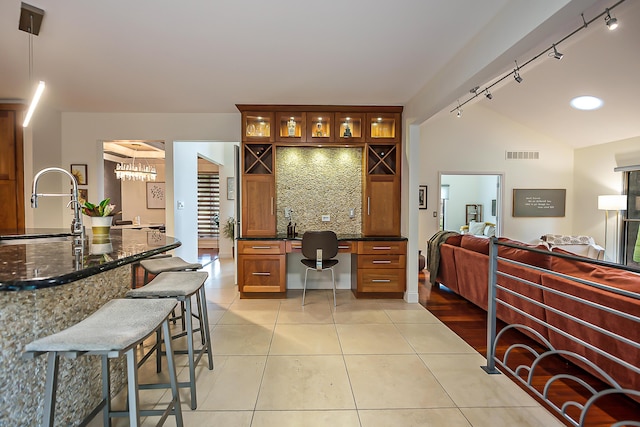 3185 Shadberry Ct, Saline, MI 48176 - kitchen with rail lighting, lofted ceiling, glass insert cabinets, dark stone countertops, and a breakfast bar