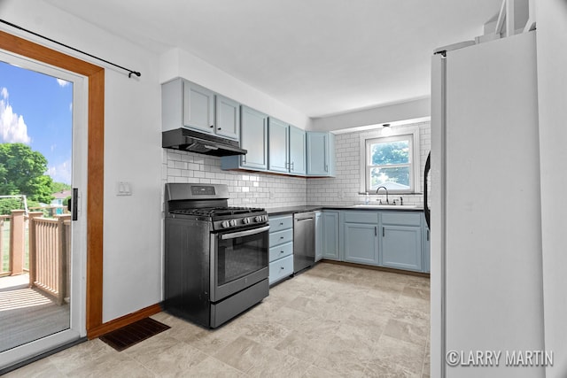 641 52nd St SE, Grand Rapids, MI 49548 - kitchen featuring appliances with stainless steel finishes, under cabinet range hood, tasteful backsplash, blue cabinetry, and dark countertops