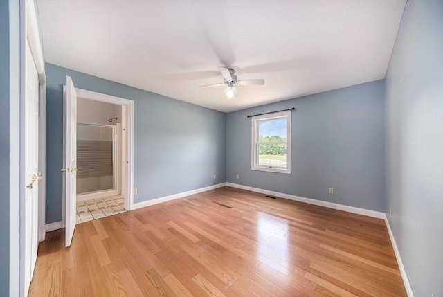 6990 Kennedy Rd, Munith, MI 49259 - unfurnished bedroom with light wood-style floors, connected bathroom, and a ceiling fan