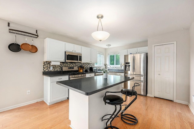 1735 Savannah Ln, Ypsilanti, MI 48198 - kitchen with appliances with stainless steel finishes, dark countertops, white cabinetry, a breakfast bar area, and light wood-style flooring