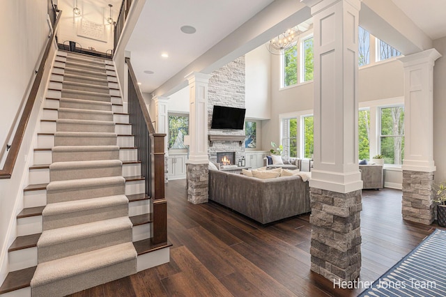 8069 Ella Terrace Ct, Rockford, MI 49341 - living room featuring decorative columns, dark wood-type flooring, a towering ceiling, a fireplace, and stairs