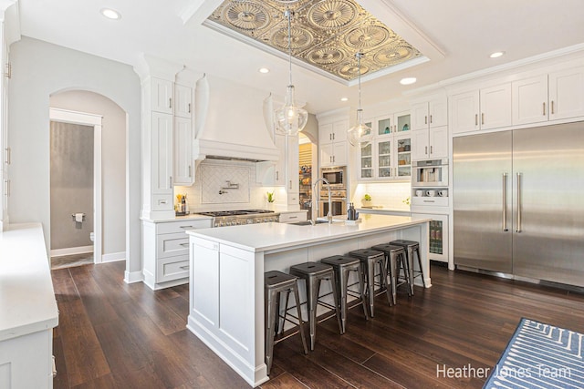 8069 Ella Terrace Ct, Rockford, MI 49341 - kitchen with built in appliances, arched walkways, custom exhaust hood, white cabinetry, and recessed lighting