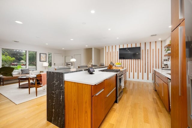 4330 Eastgate Dr, Ann Arbor, MI 48103 - kitchen with stainless steel gas range oven, light wood finished floors, brown cabinets, open floor plan, and a center island