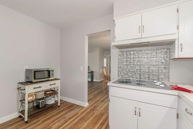 1736 Glenvale Dr SW, Wyoming, MI 49519 - kitchen with stainless steel microwave, black electric stovetop, under cabinet range hood, light wood finished floors, and white cabinets