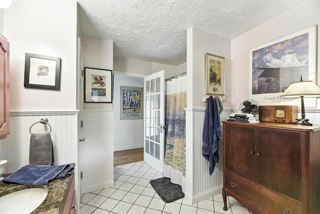 8454 Stickles Rd, Three Oaks, MI 49128 - full bathroom featuring vanity, tile patterned floors, a wainscoted wall, french doors, and a textured ceiling