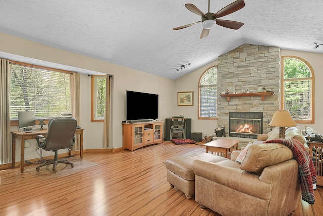 4792 Forest Vale Dr, Pierson, MI 49339 - living room featuring a textured ceiling, lofted ceiling, ceiling fan, light wood finished floors, and a stone fireplace