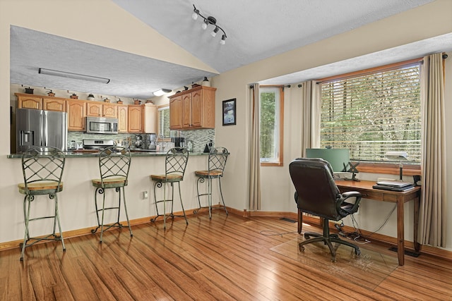 4792 Forest Vale Dr, Pierson, MI 49339 - kitchen featuring appliances with stainless steel finishes, a textured ceiling, lofted ceiling, light wood-style floors, and a breakfast bar area