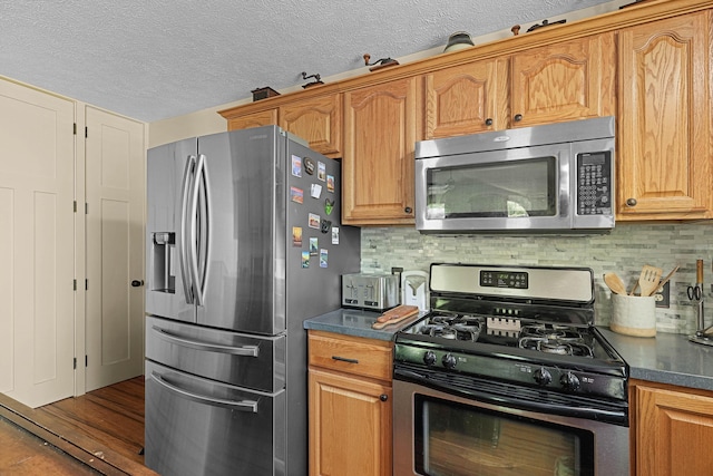 4792 Forest Vale Dr, Pierson, MI 49339 - kitchen featuring stainless steel appliances, dark countertops, backsplash, a textured ceiling, and wood finished floors