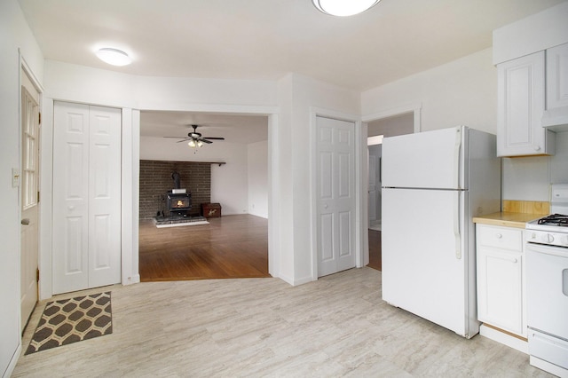 105 S Emerson Lake Rd, Branch, MI 49402 - kitchen with white appliances, a wood stove, white cabinets, light wood-style floors, and light countertops