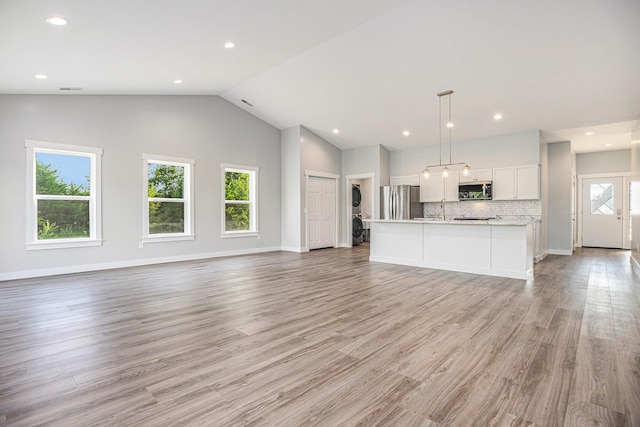 57860 James Dr, Three Rivers, MI 49093 - unfurnished living room featuring stacked washing machine and dryer, lofted ceiling, light wood-type flooring, and recessed lighting