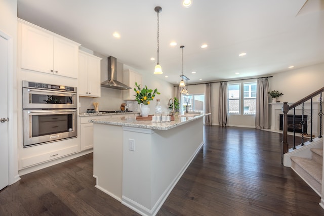 2763 Polson St, Ann Arbor, MI 48105 - kitchen with wall chimney exhaust hood, stainless steel appliances, dark wood finished floors, a center island with sink, and white cabinetry