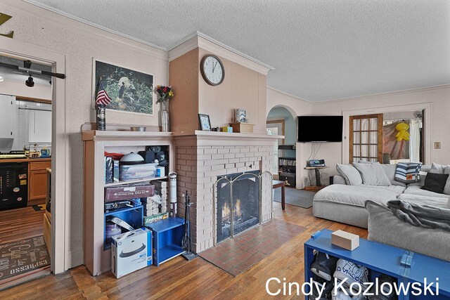 187 Centennial St, Sparta, MI 49345 - living room with crown molding, a textured ceiling, wood finished floors, a brick fireplace, and arched walkways