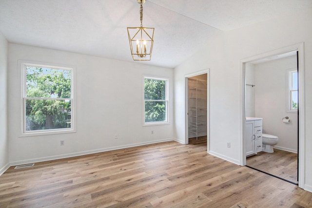 1882 Whistle Stop Dr SE, Grand Rapids, MI 49508 - unfurnished bedroom featuring a spacious closet, multiple windows, a chandelier, and light wood-type flooring