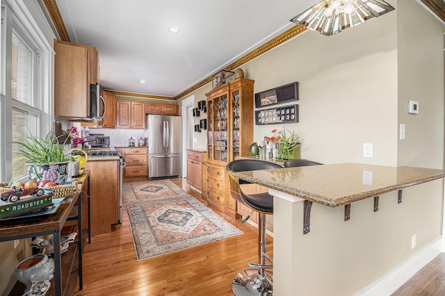 6667 W River Rd NE, Belmont, MI 49306 - kitchen featuring stainless steel appliances, a peninsula, light wood-style flooring, brown cabinets, and a breakfast bar