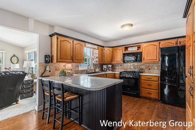 1033 Lumina Dr, Jenison, MI 49428 - kitchen with black appliances, a peninsula, dark wood finished floors, a kitchen breakfast bar, and tasteful backsplash