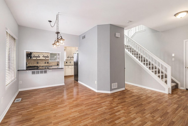 7400 Willow Creek Dr, Ypsilanti, MI 48197 - kitchen featuring stainless steel appliances, light wood finished floors, dark countertops, backsplash, and hanging light fixtures