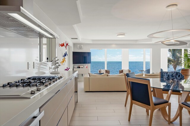 kitchen featuring stainless steel gas cooktop, wall chimney range hood, white cabinets, and decorative light fixtures