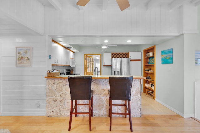 kitchen featuring a peninsula, stainless steel fridge with ice dispenser, gas range, ceiling fan, and white microwave