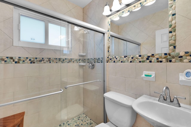 bathroom with a sink, toilet, a stall shower, and tile walls