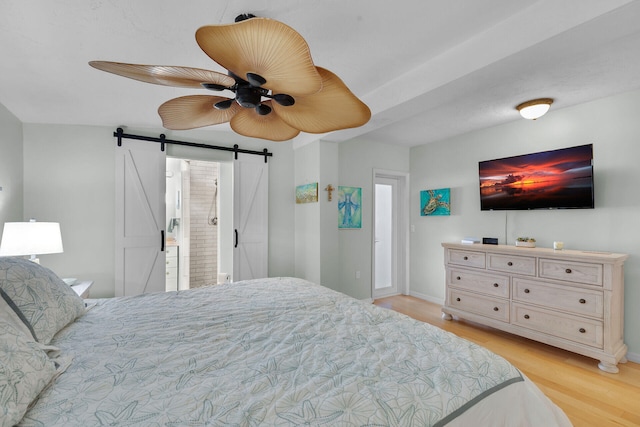 bedroom featuring light wood finished floors, ceiling fan, a barn door, and baseboards