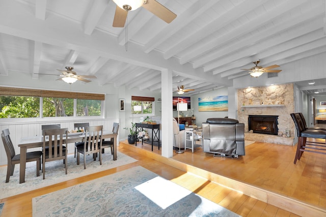 dining room featuring a fireplace, ceiling fan, wood-type flooring, and vaulted ceiling with beams